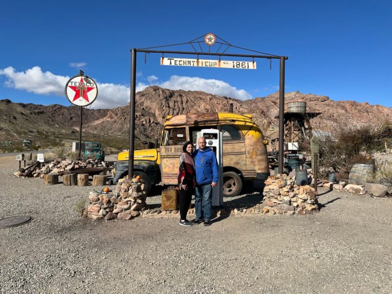 Explore Nevada’s desert near Las Vegas! A couple poses by a vintage yellow car at Techatticup 1861. Perfect for ATV tours and ghost town sightseeing.