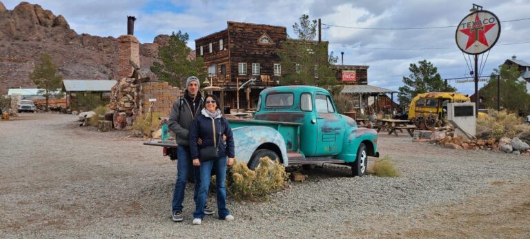 Two people smile by a vintage turquoise truck in a Nevada desert near Las Vegas, with ghost town sights and RZR rides nearby.