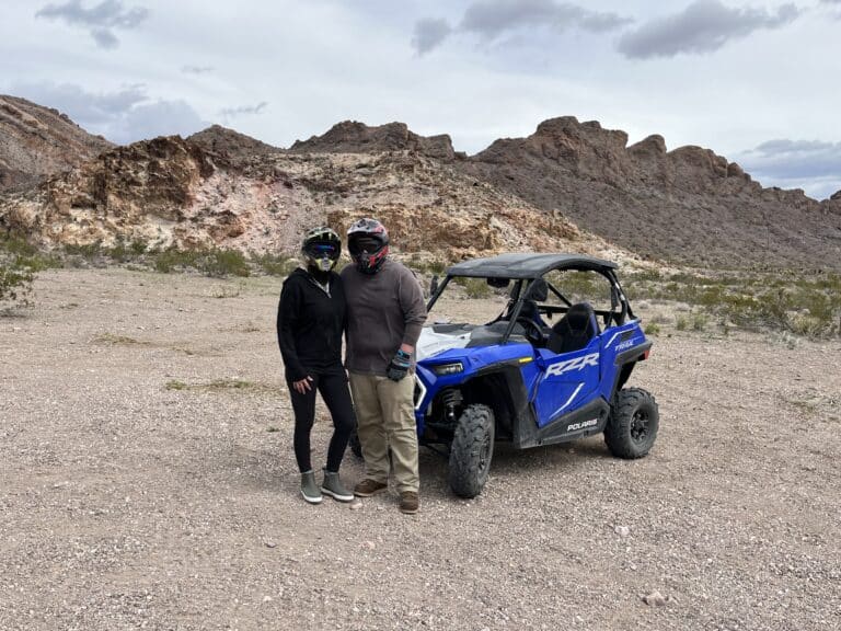 Explore Nevadas rocky desert near Las Vegas with thrilling RZR off-road rides. Two adventurers gear up beside their blue vehicle.