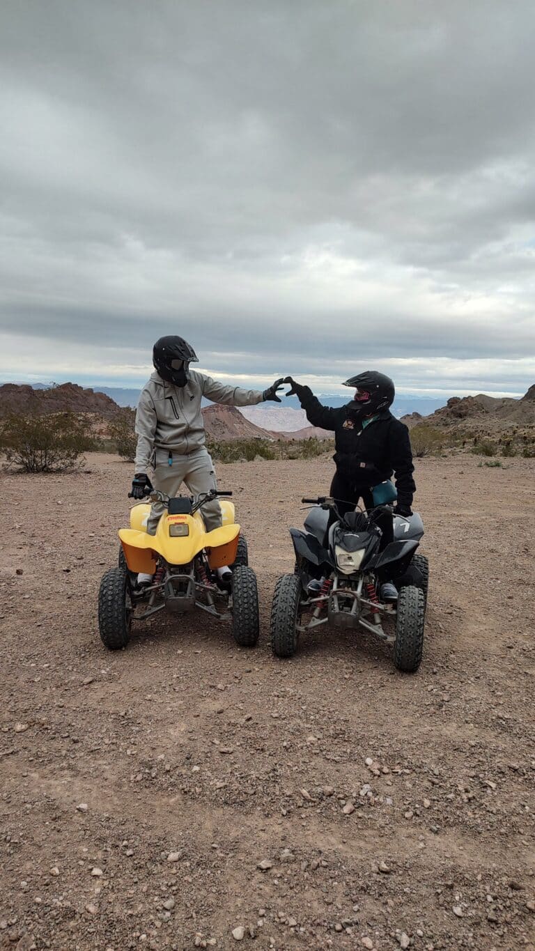 Two adventurers high-five on vibrant yellow and black ATVs in Nevadas desert with an overcast sky, near Las Vegas and Colorado River.