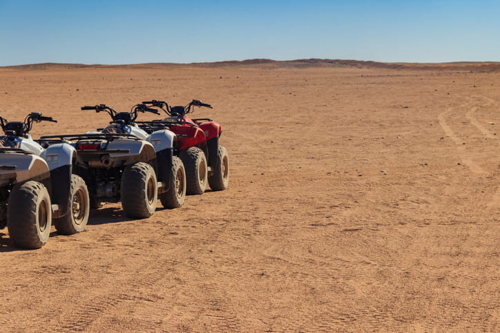 3 ATVs parked in a row out in the desert.