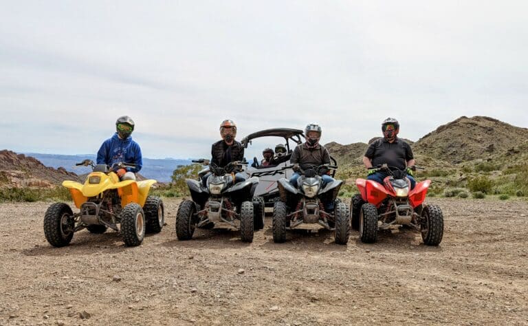 Experience thrilling ATV tours near the Colorado River, Nevada! Four ATVs and an RZR line up on rocky terrain with stunning hill views.