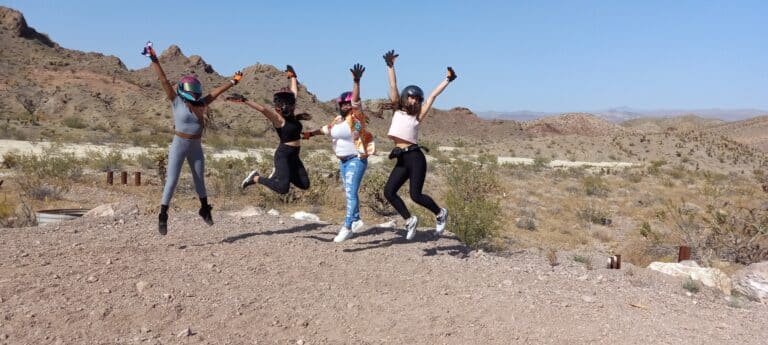 Adventurers in Nevada Desert: Thrill-seekers in helmets leap joyously, showcasing ATV tours near Las Vegas and the Colorado Rivers beauty.