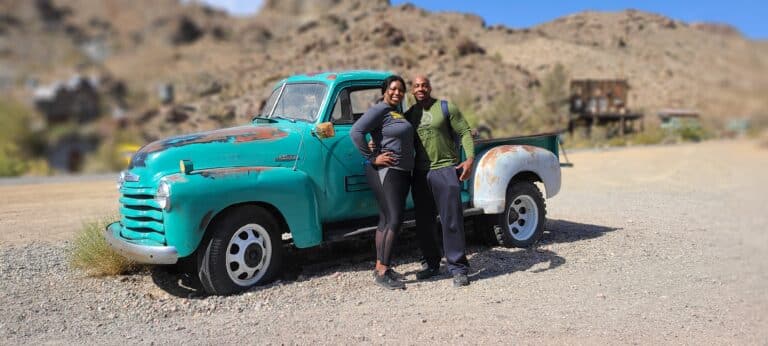 Couple smiles by rusty turquoise pickup in Nevadas rocky desert near Las Vegas - ideal for ATV tours and Colorado River views.