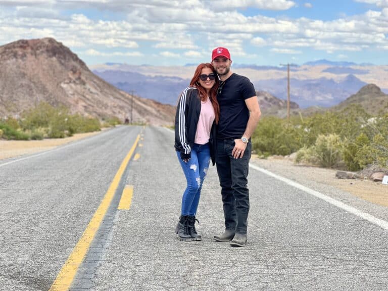 Couple smiles on a deserted Nevada road near Colorado River, under a partly cloudy sky. Ideal for ATV tours and RZR off-road adventures.