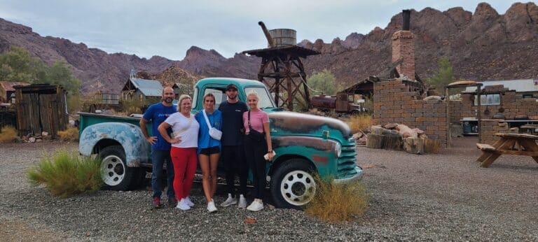 Five friends smile by a vintage turquoise truck in a Nevada desert, perfect for RZR rides. Explore near Las Vegas & the Colorado River settings!.