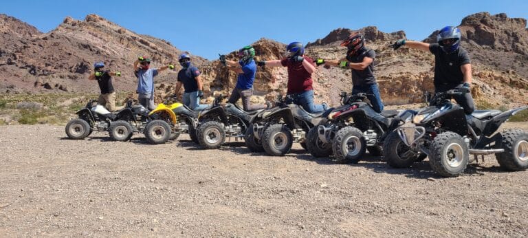 Adventure-seekers in Nevada enjoy ATV tours near Las Vegas, posing by the Colorado River with rocky hills and blue skies.