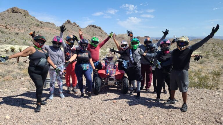 A lively group in helmets and colorful gear poses by their ATV for an exciting Nevada adventure near Las Vegas rocky desert hills.
