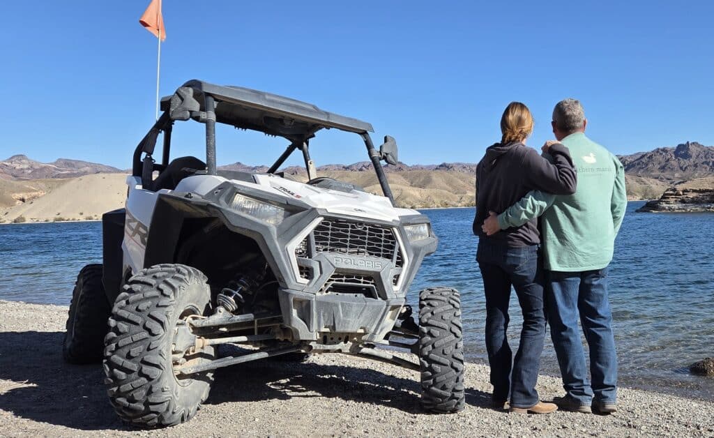 A couple by the Colorado River near Las Vegas stands by a white ATV with orange flag, enjoying Nevada’s scenic off-road adventure.