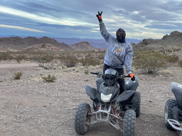 Explore Nevadas desert on a Las Vegas ATV tour! Peace sign adventure with orange gear amid rocky hills and cloudy skies near Colorado River.