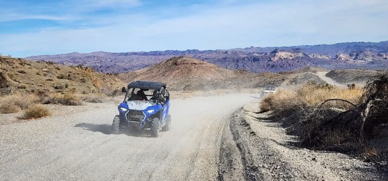 A blue ATV maneuvers a dusty trail in Nevadas desert near Las Vegas, with arid mountains hinting at ghost town sightseeing.