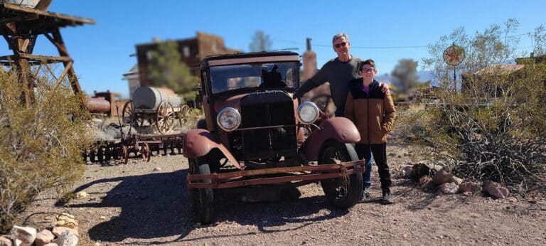 Two people pose by a vintage car in Nevadas sunlit Ghost Town, near Las Vegas, ideal for ATV tours and Colorado River fun.