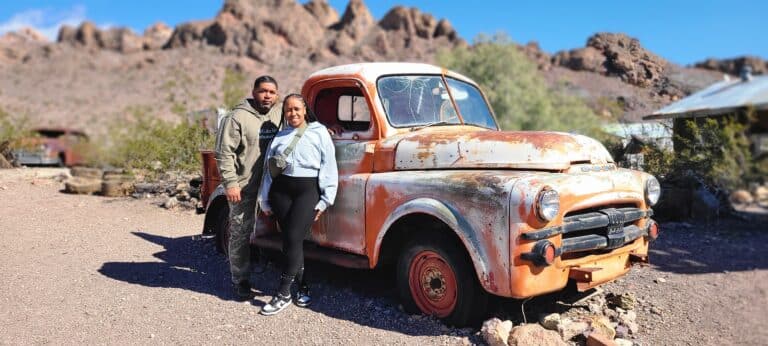 A couple smiles by a rusty orange truck in Nevada’s desert, near Las Vegas, perfect for ghost town sightseeing and RZR off-road rides.