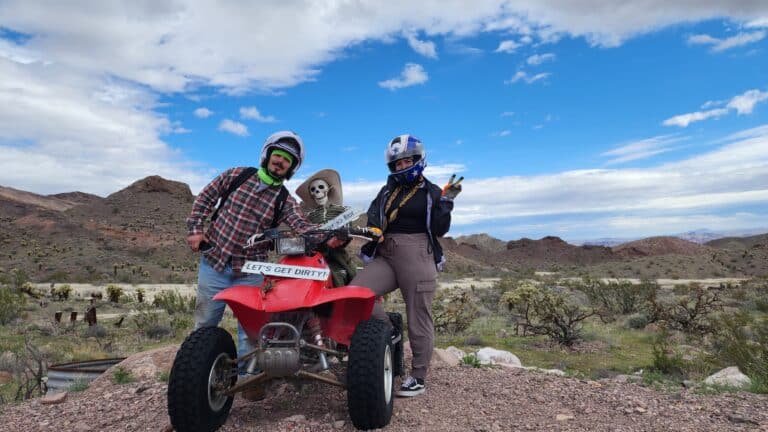 Three helmeted adventurers in a skeleton costume with an ATV in Nevadas desert, ready for thrilling RZR off-road rides near Las Vegas.