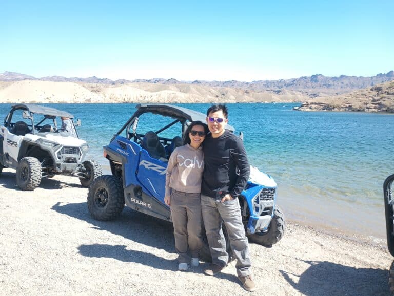 A couple enjoys an RZR off-road adventure by a lake near Las Vegas. Smiling under Nevadas blue skies, theyre ready for Ghost Town sightseeing.