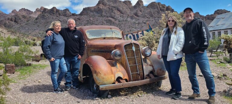 Four adventurers pose by a vintage car in Nevadas desert, ready for RZR off-road rides and ATV tours near Las Vegas and the Colorado River.