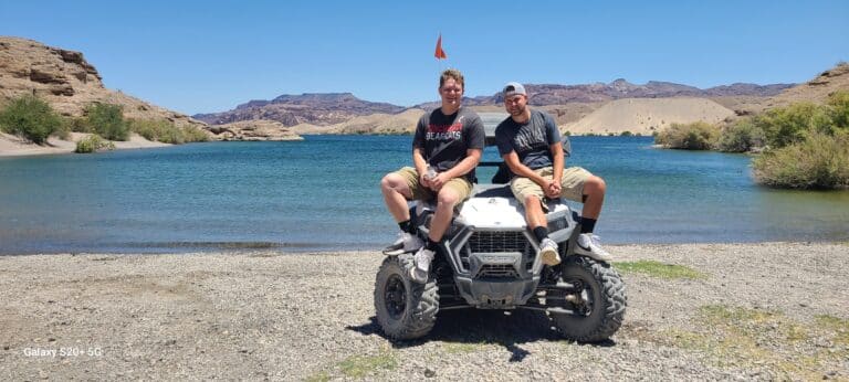 Two smiling adventurers on a white ATV at a Nevada lake enjoy a Colorado River tour near Las Vegas—perfect for an ATV or RZR ride.