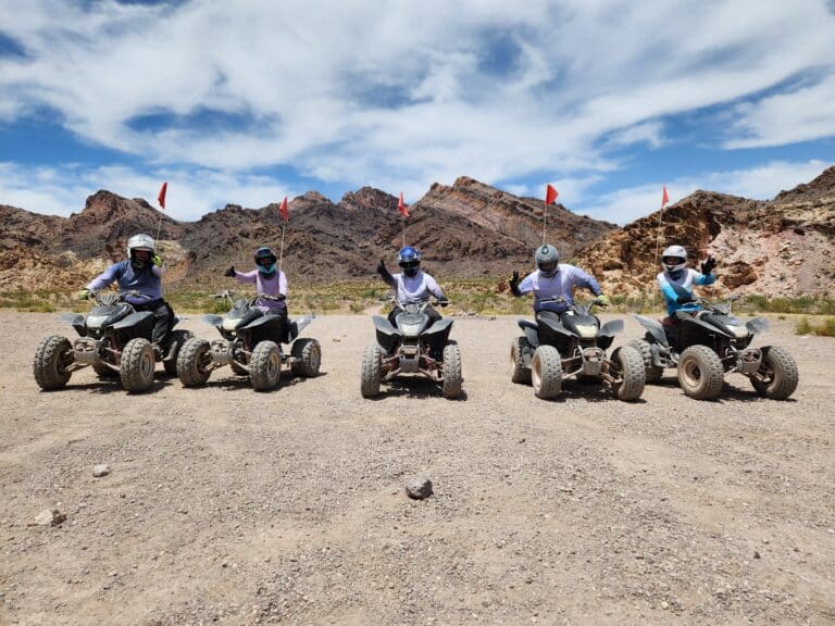 Five adventurers on quad bikes in Nevadas stunning desert, near the Colorado River, pose with peace signs and red flags on an ATV tour.