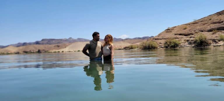 A couple stands waist-deep in a peaceful lake, surrounded by Nevadas hills—experience this serenity on a Colorado River tour near Las Vegas.