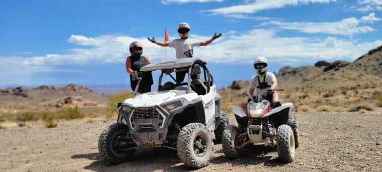Thrill-seekers in helmets pose with an ATV near a quad bike, celebrating their Las Vegas Colorado River ATV tour in the Nevada desert.