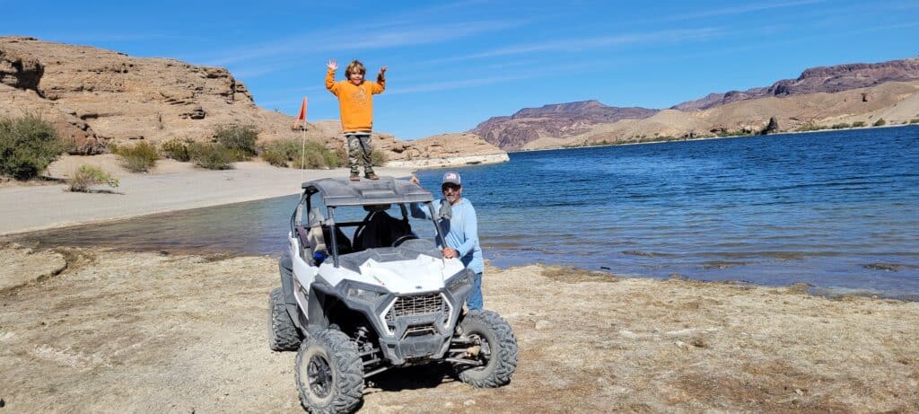 A child in an orange shirt triumphantly stands on a white ATV by the Colorado River near Las Vegas, enjoying Nevadas outdoor adventures.
