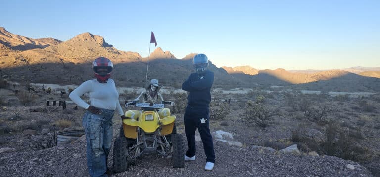 Adventure seekers in helmets pose with a yellow ATV in the Nevada desert near Las Vegas, ready for thrilling ATV tours.