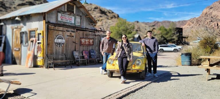 Three people pose by a vintage yellow car in a Nevada ghost town, near Las Vegas and the Colorado River, ideal for RZR off-road rides.