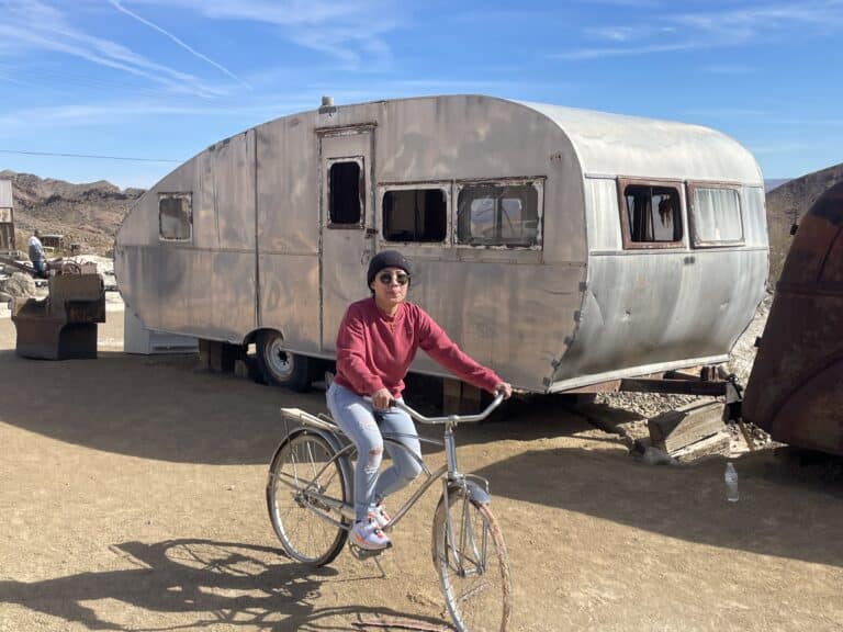 In Nevadas desert near Las Vegas, a cyclist in a red sweater rides past a shiny trailer. Perfect day for Colorado River tours or ATV adventures!.