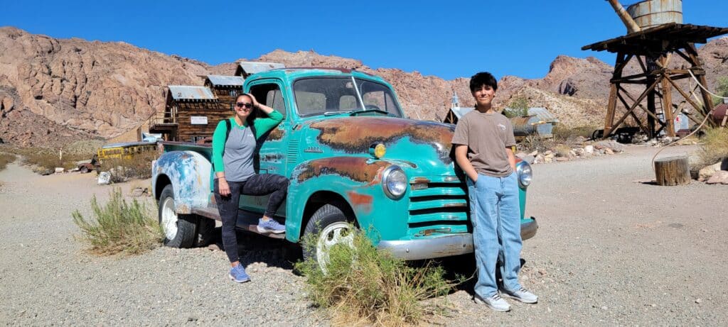 Couple poses with a vintage turquoise truck near Las Vegas; discover Nevadas desert charm on Ghost Town sightseeing or ATV tours.