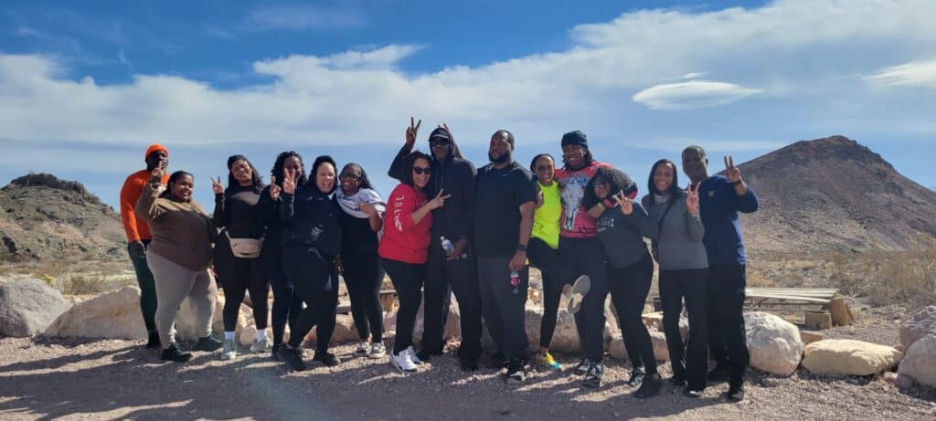 Cheerful group by Nevadas desert backdrop near Las Vegas, flashing peace signs in bright and dark attire during an ATV tour.