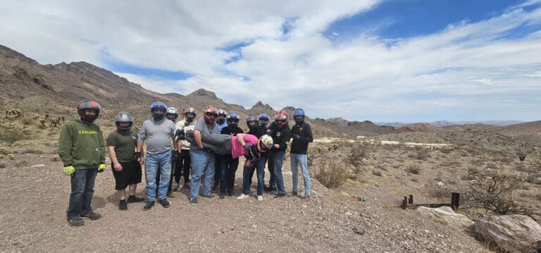 A group of ten in helmets explore Nevadas rocky desert near Las Vegas. One holds a child with mountains visible, perfect for ATV tours.