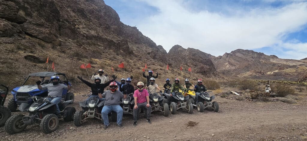Thrill-seekers in helmets cheer on ATVs near Nevadas rugged mountains. Join Las Vegas ATV tours or Colorado River RZR rides today!.