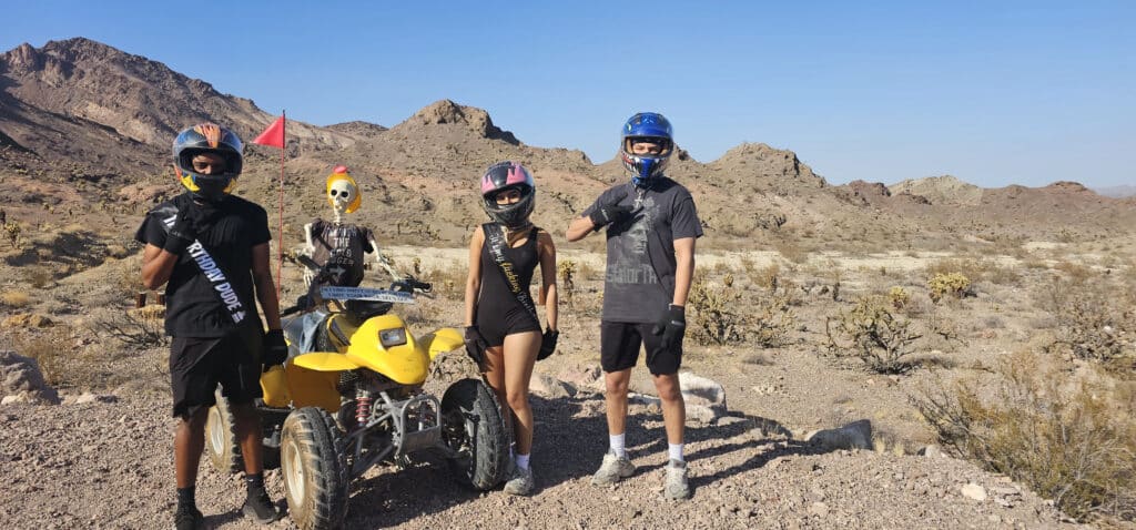 Four adventurers in helmets pose by a yellow ATV in Nevadas rocky desert near Las Vegas, perfect for thrilling RZR off-road rides.