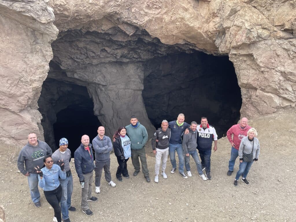 Thirteen visitors pose by Nevadas cave-like rocks near Colorado River, enjoying ATV tours and Ghost Town sights near Las Vegas.