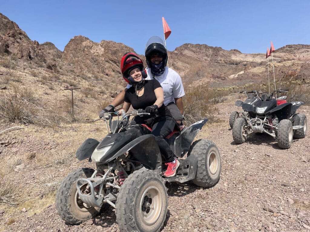 ATV adventure in Nevadas rocky desert: A rider in black and red helmet with a smiling passenger explores near Las Vegas. Azure sky.