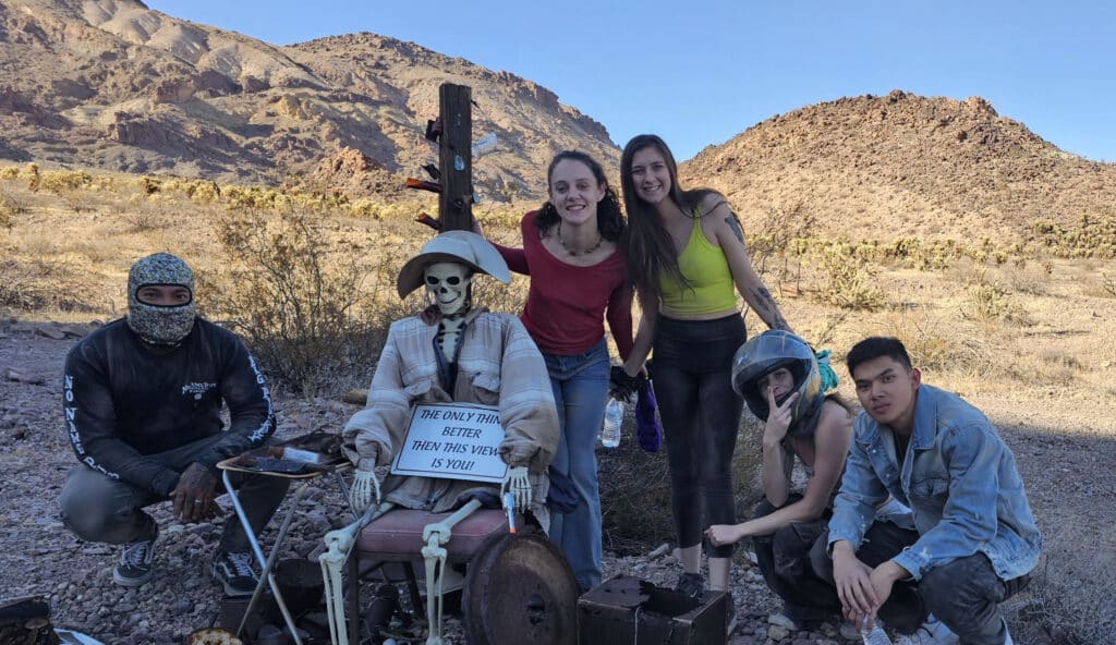 Group poses near Las Vegas in a rocky Nevada desert with a dressed skeleton in a wheelchair after an ATV tour adventure.
