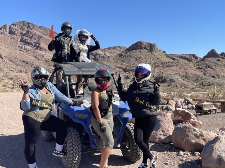 Bridal party posing by RZR off-road vehicle in Nevada desert near Las Vegas, ready for ATV tour and Ghost Town sightseeing adventure.