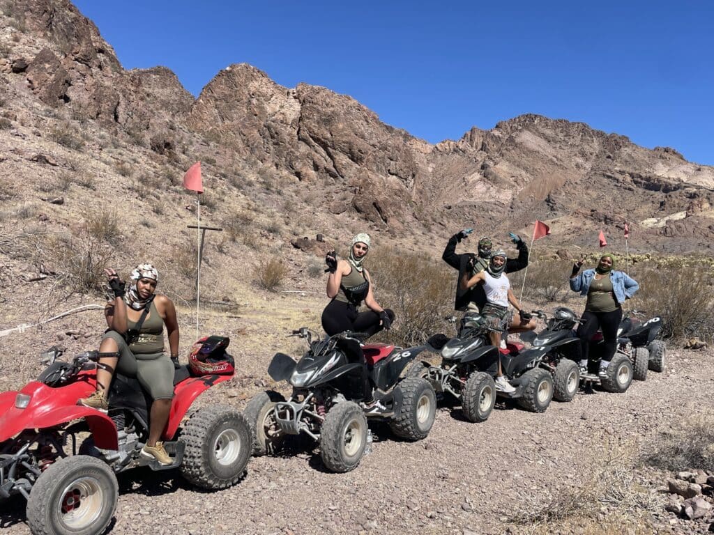Four friends enjoy an ATV tour near Las Vegas, raising arms on Nevada’s rocky trails with mountains and a clear sky in the background.