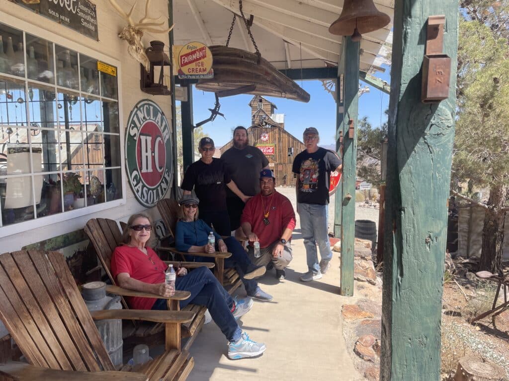 Six people pose on a rustic Nevada porch near Las Vegas, with vintage signs—perfect for Colorado River ghost town sightseeing photos!.