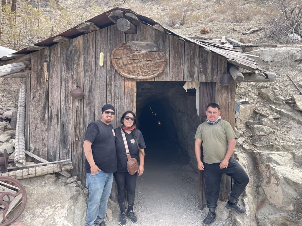 Smiling visitors at Eldorado Mine near Las Vegas, Nevada, pose by vintage mining gear—perfect for ATV and Ghost Town tours.