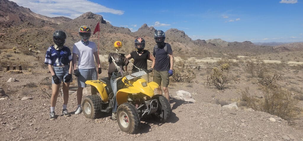 Adventurers in helmets explore a Nevada desert trail on an ATV near Las Vegas, with mountains and the Colorado River views.