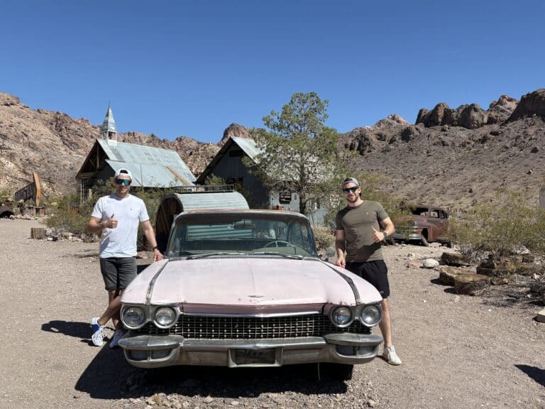 Two men in casual wear pose by a vintage pink car in a Nevada ghost town near Las Vegas, perfect for ATV and RZR tours.