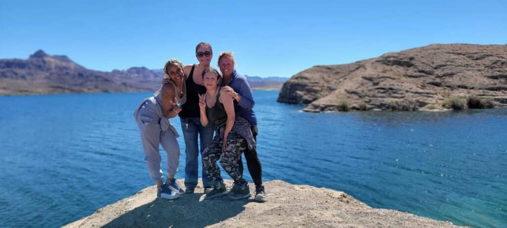 Happy group enjoys RZR ATV tour at a rocky outcrop near a blue lake with mountain views, just outside Las Vegas, Nevada, by the Colorado River.