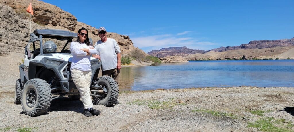 Adventurers in light gear pose by an ATV on the rocky Colorado River shore near Las Vegas, Nevada—ideal for RZR tours and sightseeing.
