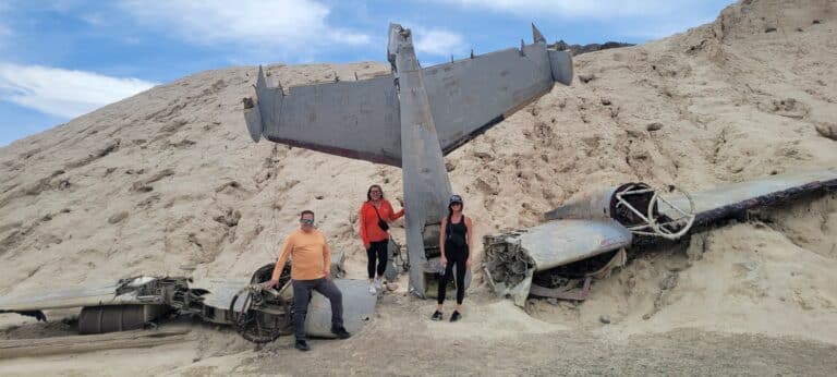 Three stand by a crashed airplane in Nevada’s desert near Las Vegas, perfect for ATV tours and ghost town adventures.