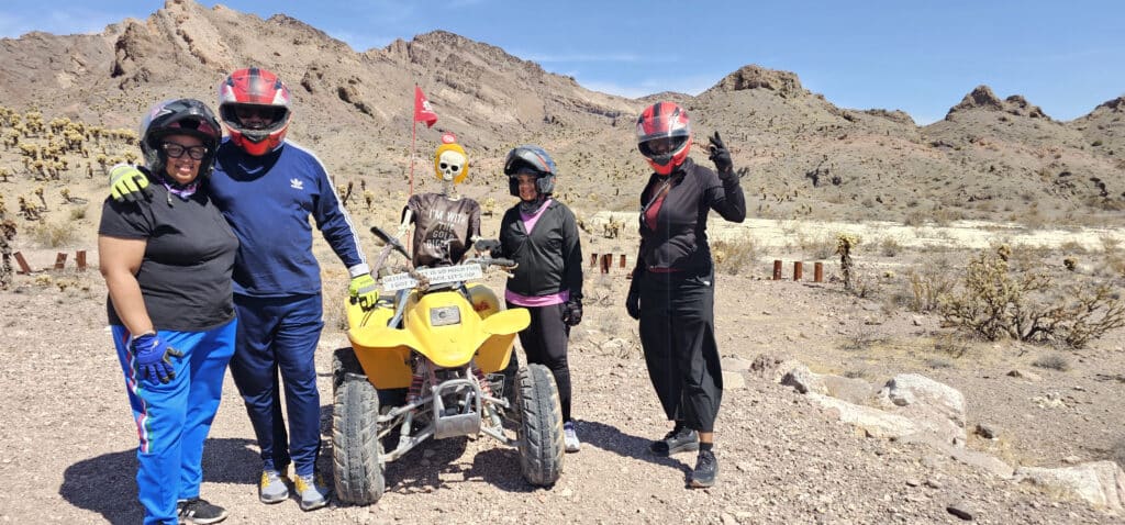 Adventurers in helmets pose by a yellow ATV and skeleton prop during an ATV tour near Las Vegas and the Colorado River, Nevada.