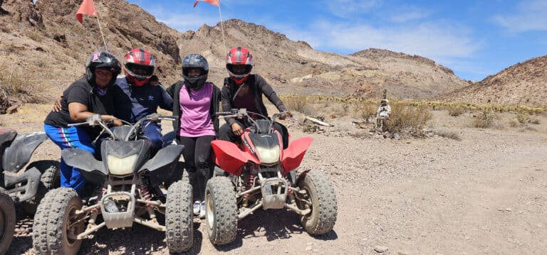 Smiling group on ATVs enjoys a Las Vegas desert tour near the Colorado River with Nevada’s mountains in the background.