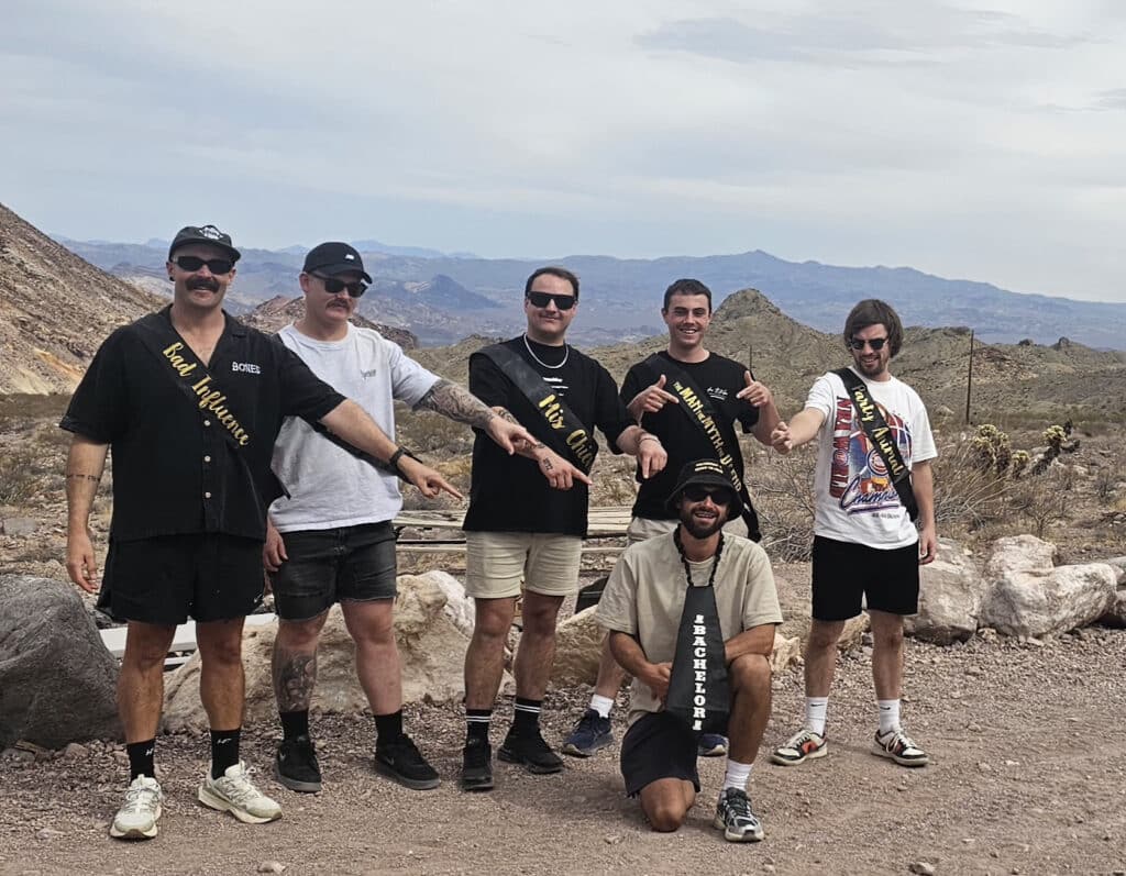 Six friends pose on rocky Nevada terrain near the Colorado River after an exciting Las Vegas RZR off-road ATV tour.