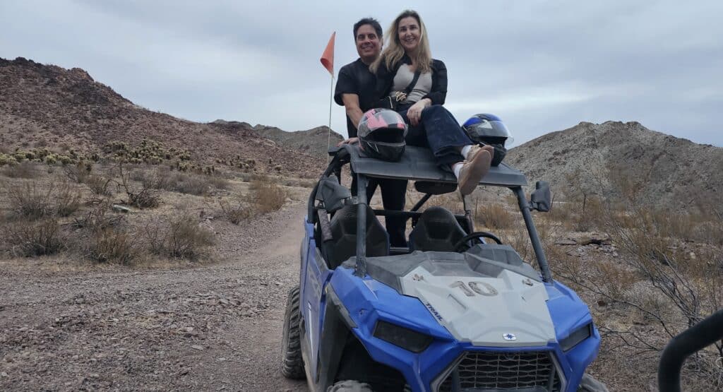 Couple atop blue ATV on a Nevada desert trail near Las Vegas, helmets ready for RZR off-road adventure by the Colorado River.