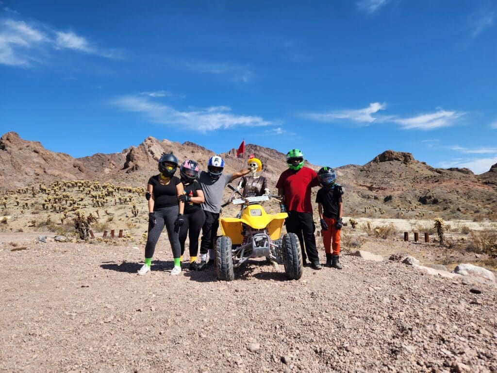 Five adventurers in helmets gather by a yellow ATV in the Nevada desert near Las Vegas on an exciting ATV tour.